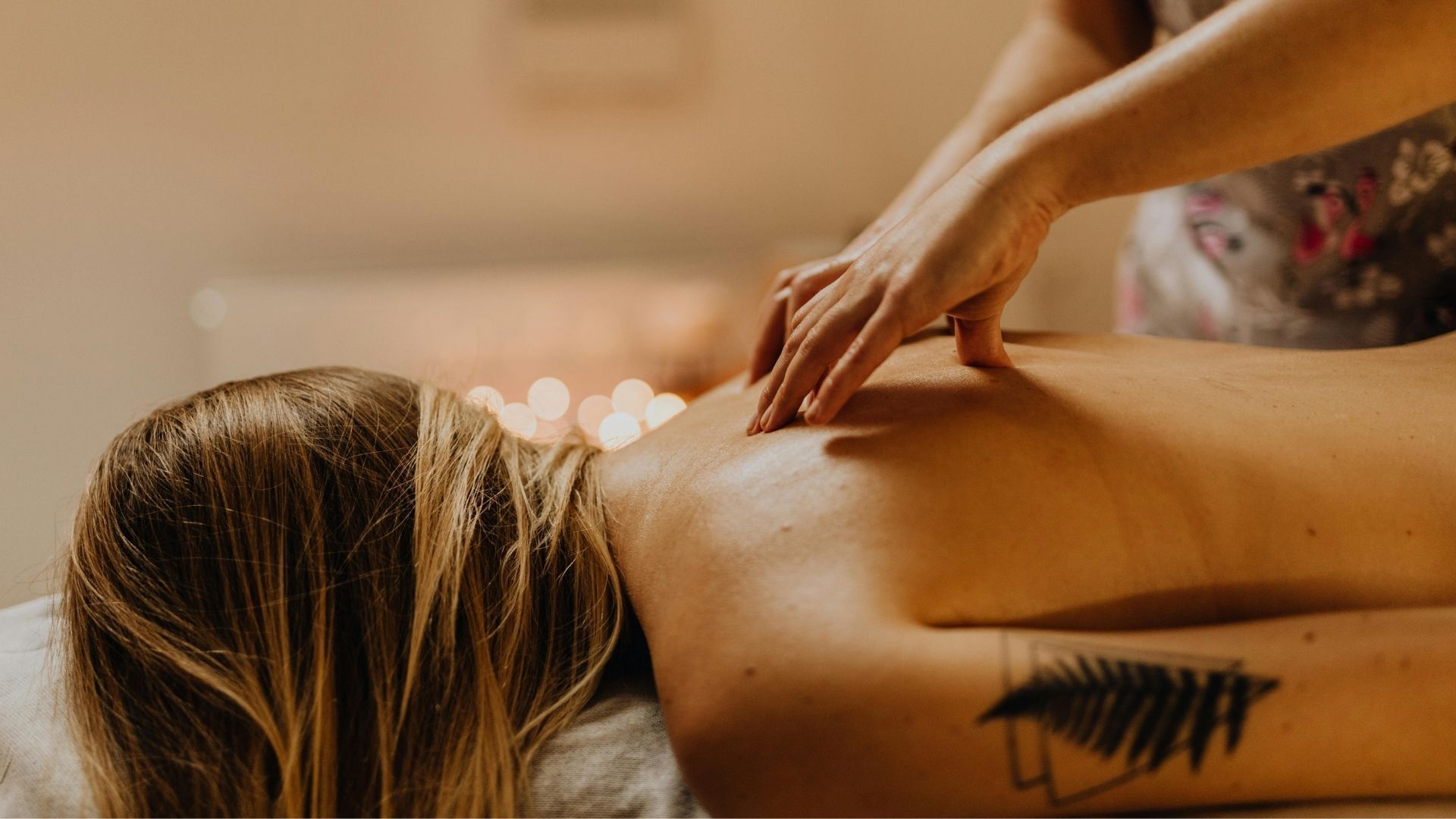 Persona recibiendo masaje de espalda; manos del masajista sobre la espalda desnuda, tatuaje visible.