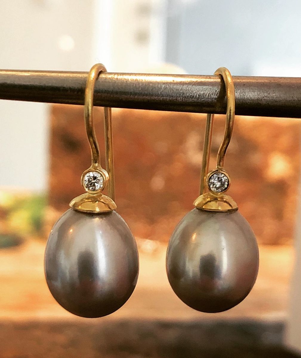 Ein Paar Ohrringe mit Perlen und Diamanten hängen an einer Metallstange.