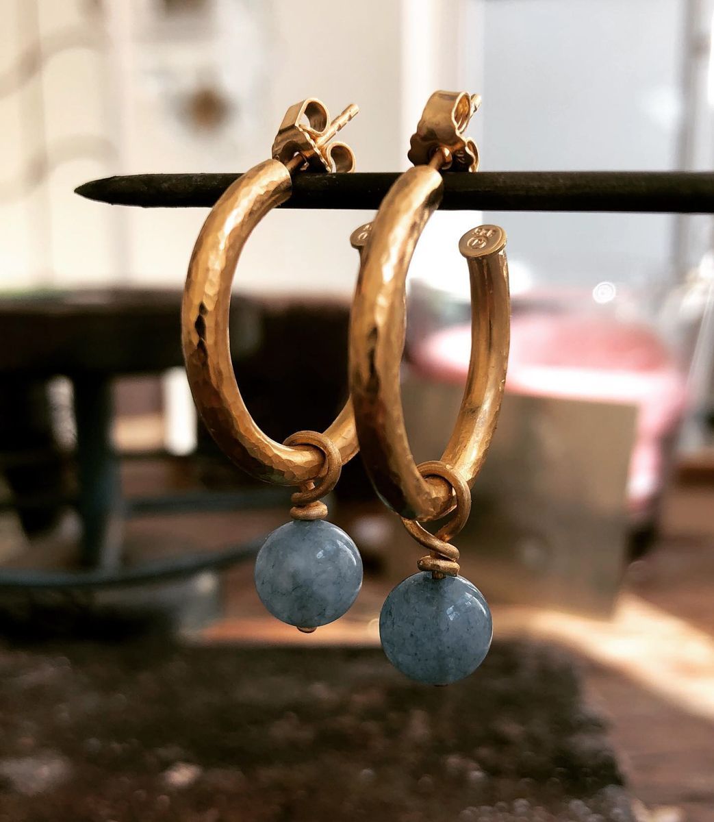 Ein Paar goldene Creolen mit einem blauen Stein daran.