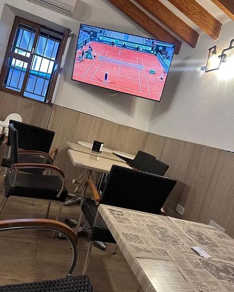 Una habitación con mesas y sillas y un televisor de pantalla plana en la pared.
