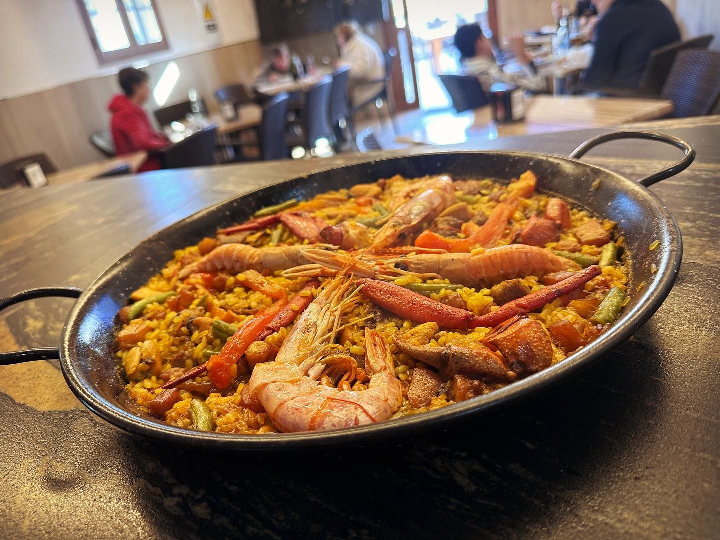 Una sartén de paella con camarones y verduras sobre una mesa en un restaurante.