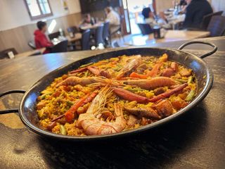 Una sartén de paella con camarones y verduras sobre una mesa en un restaurante.