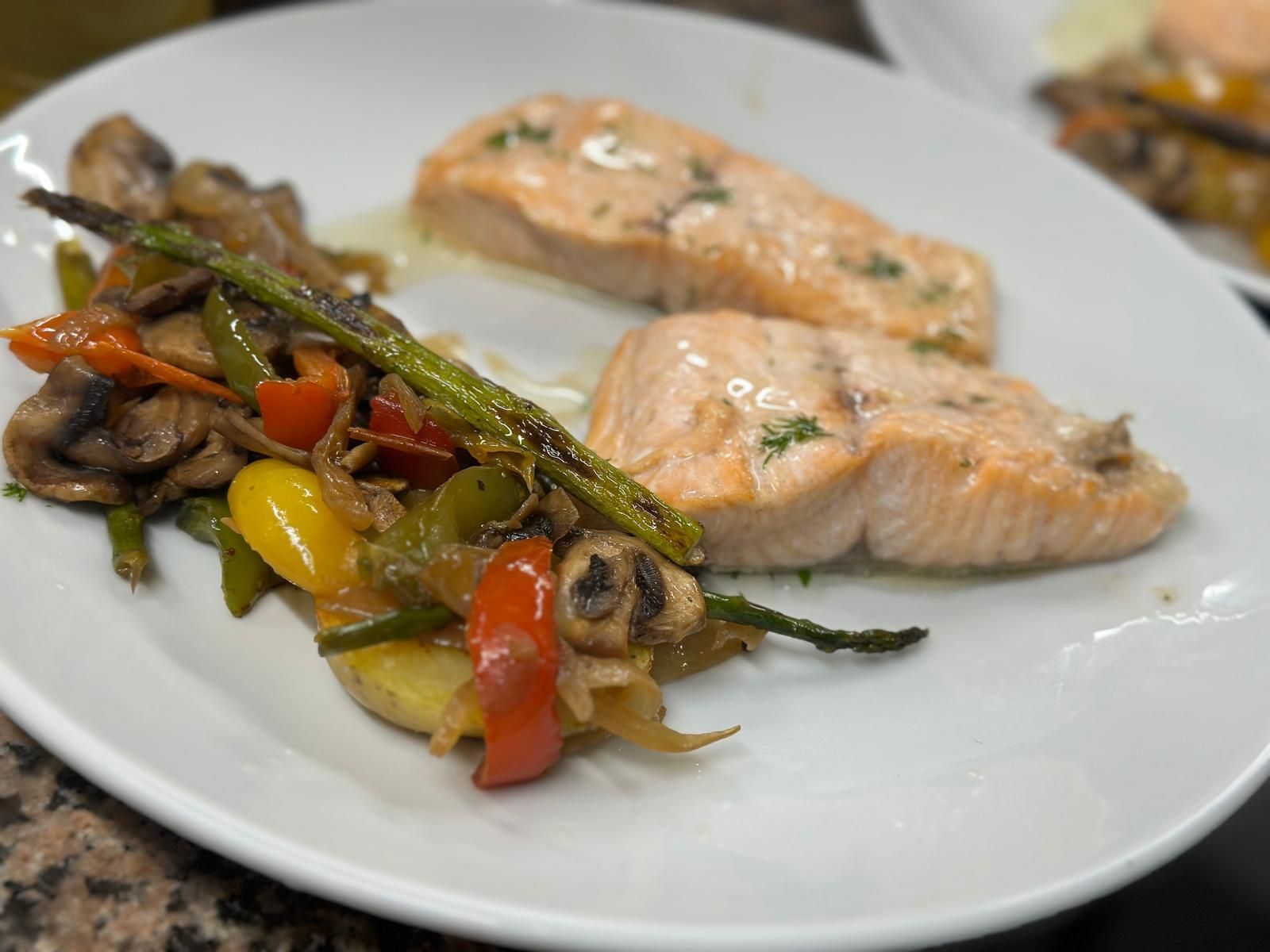 Un plato blanco cubierto con salmón y verduras sobre una mesa.