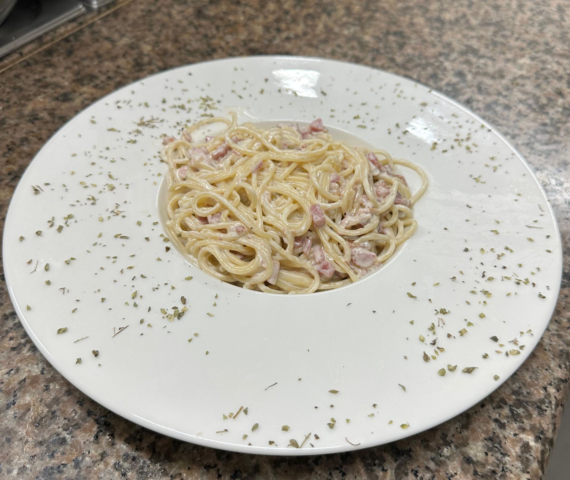 Un plato blanco cubierto con espaguetis y jamón sobre una mesa.