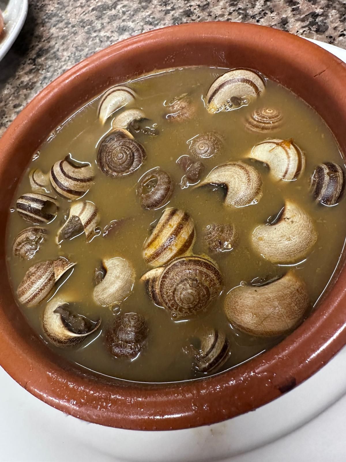 Un cuenco de caracoles en salsa sobre una mesa.