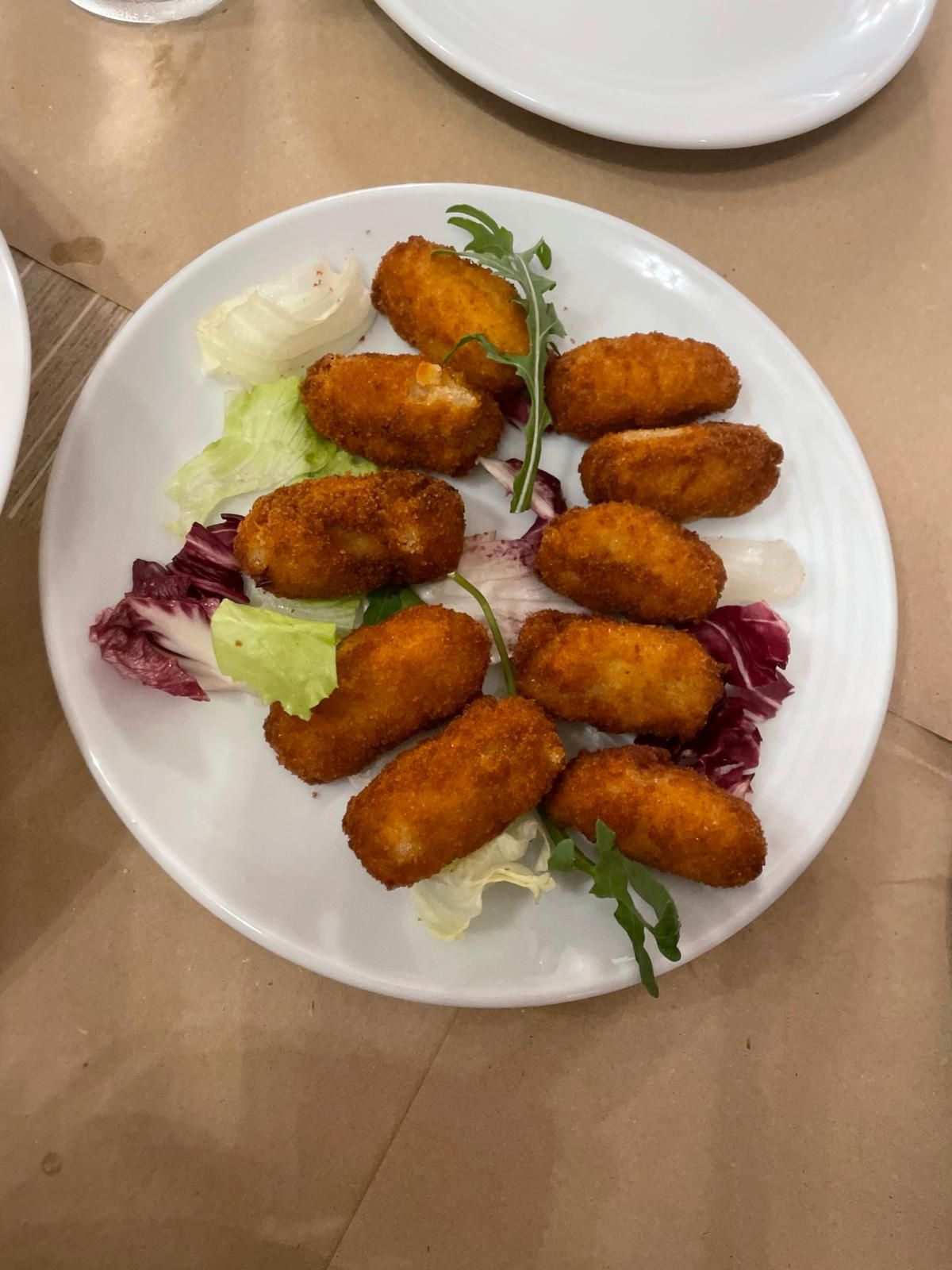 Un plato blanco cubierto con comida frita y lechuga sobre una mesa.
