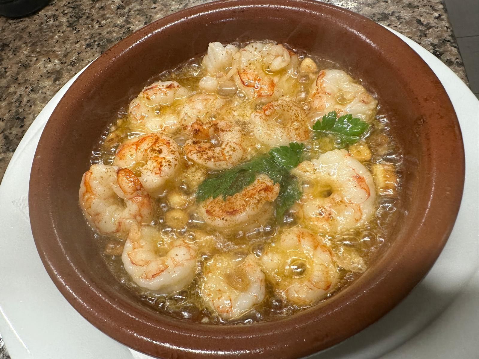 Un tazón de camarones está sobre un plato blanco.