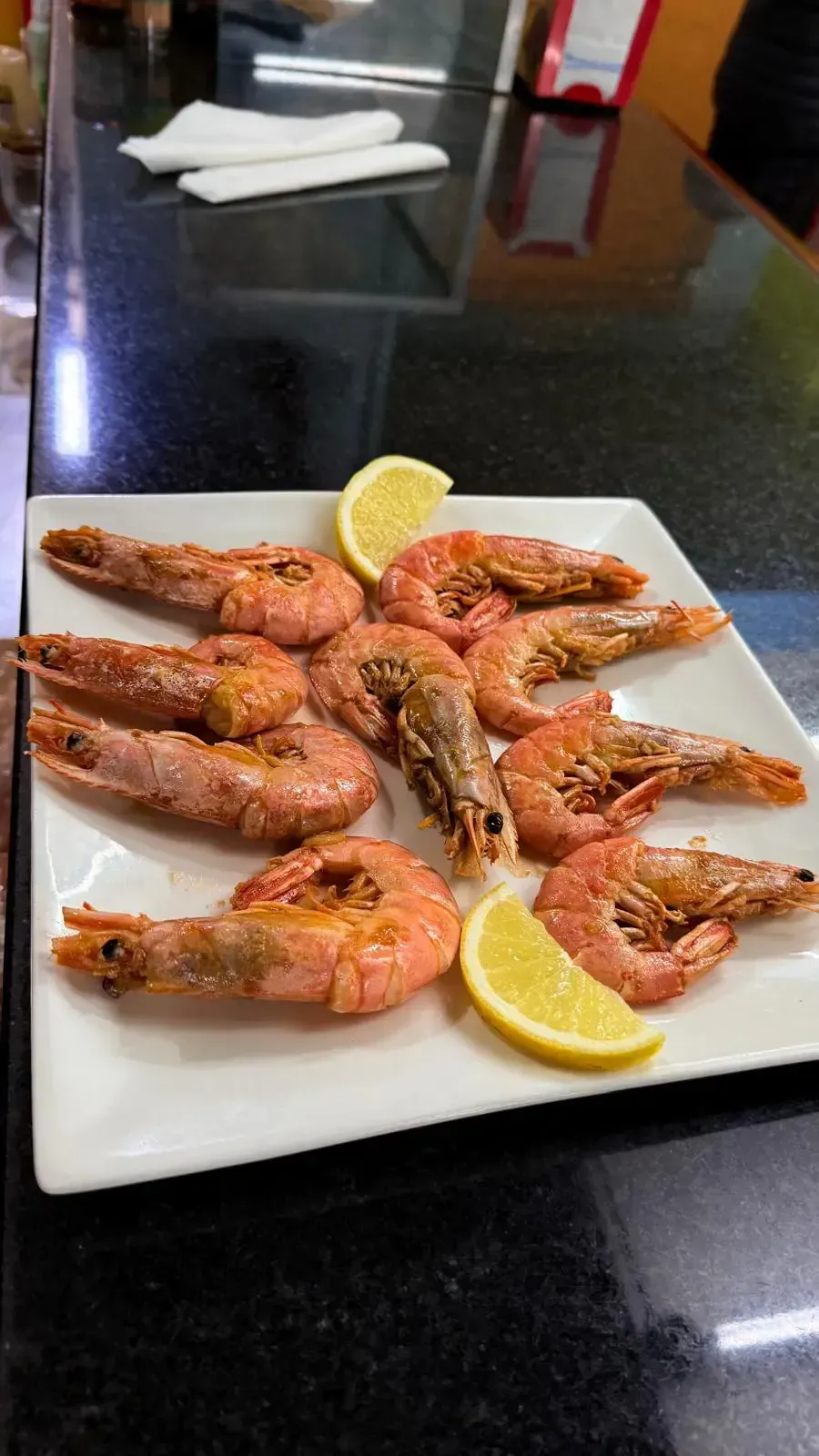 Plato de gambas a la parrilla y rodajas de limón sobre una mesa oscura de restaurante.