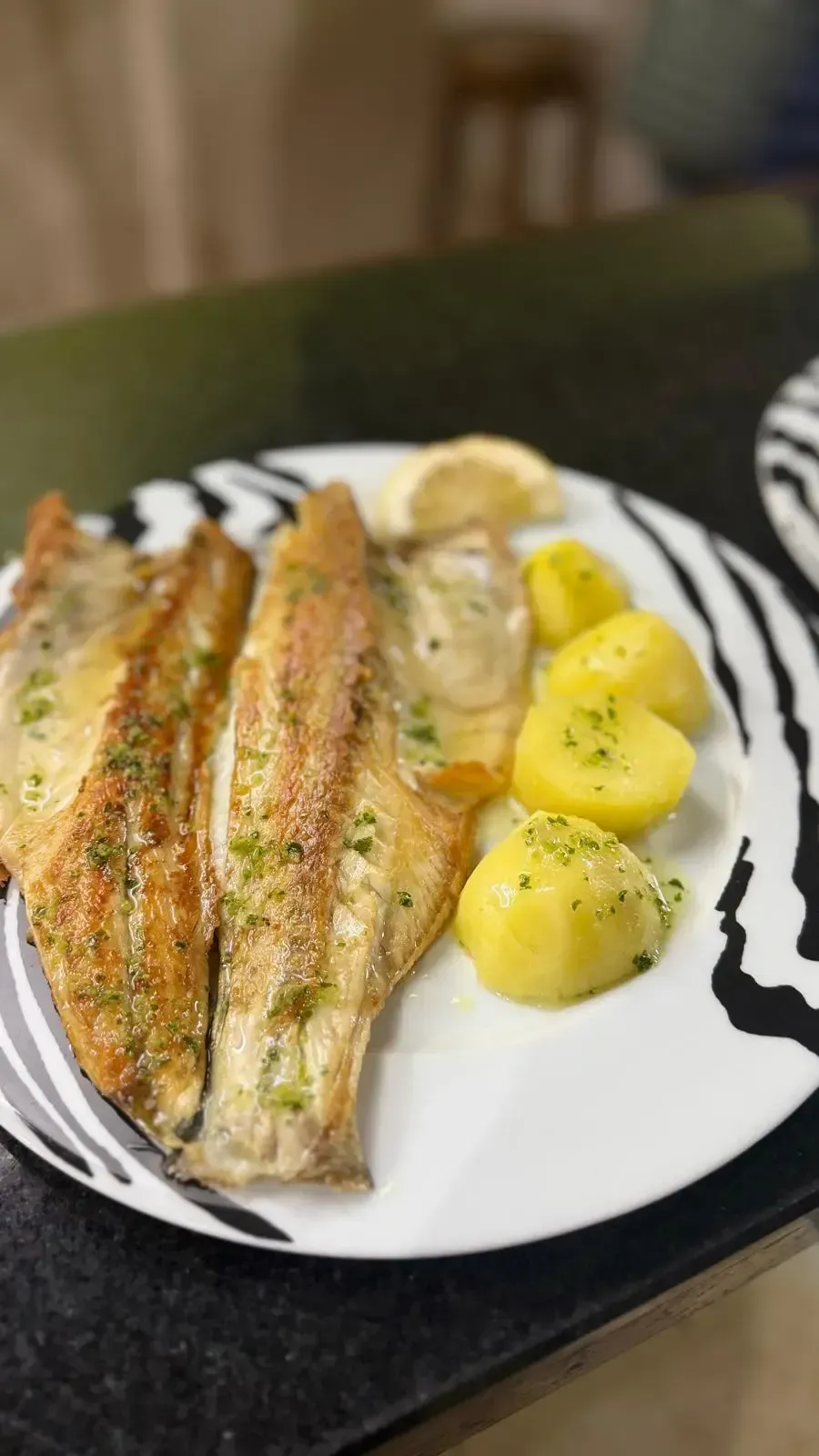 Filetes de pescado a la plancha con patatas cocidas en un plato blanco con rayas negras.