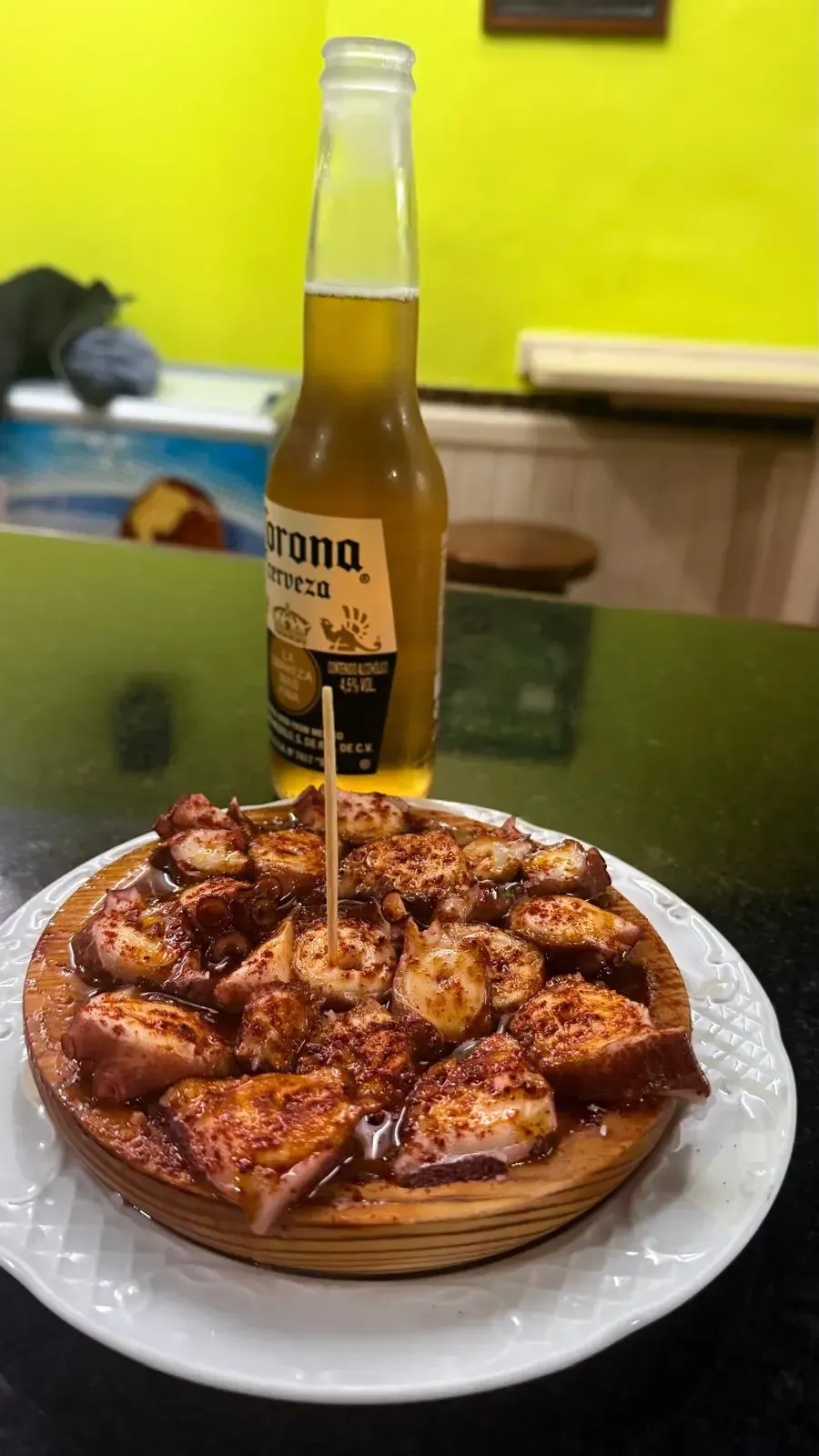 Pizza en un plato blanco con una bebida embotellada al fondo sobre una mesa.
