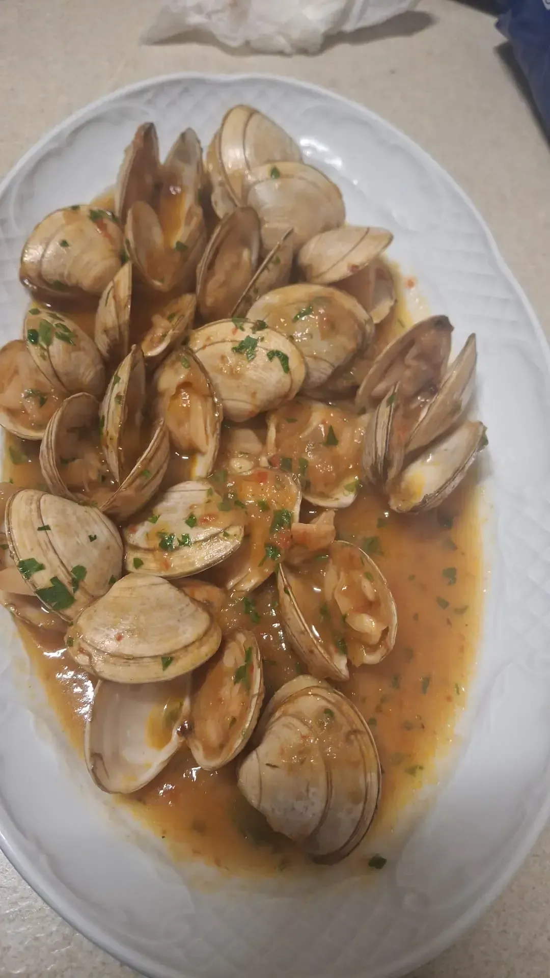 Almejas al vapor en un sabroso caldo, servidas en un plato ovalado blanco y adornadas con hierbas picadas.