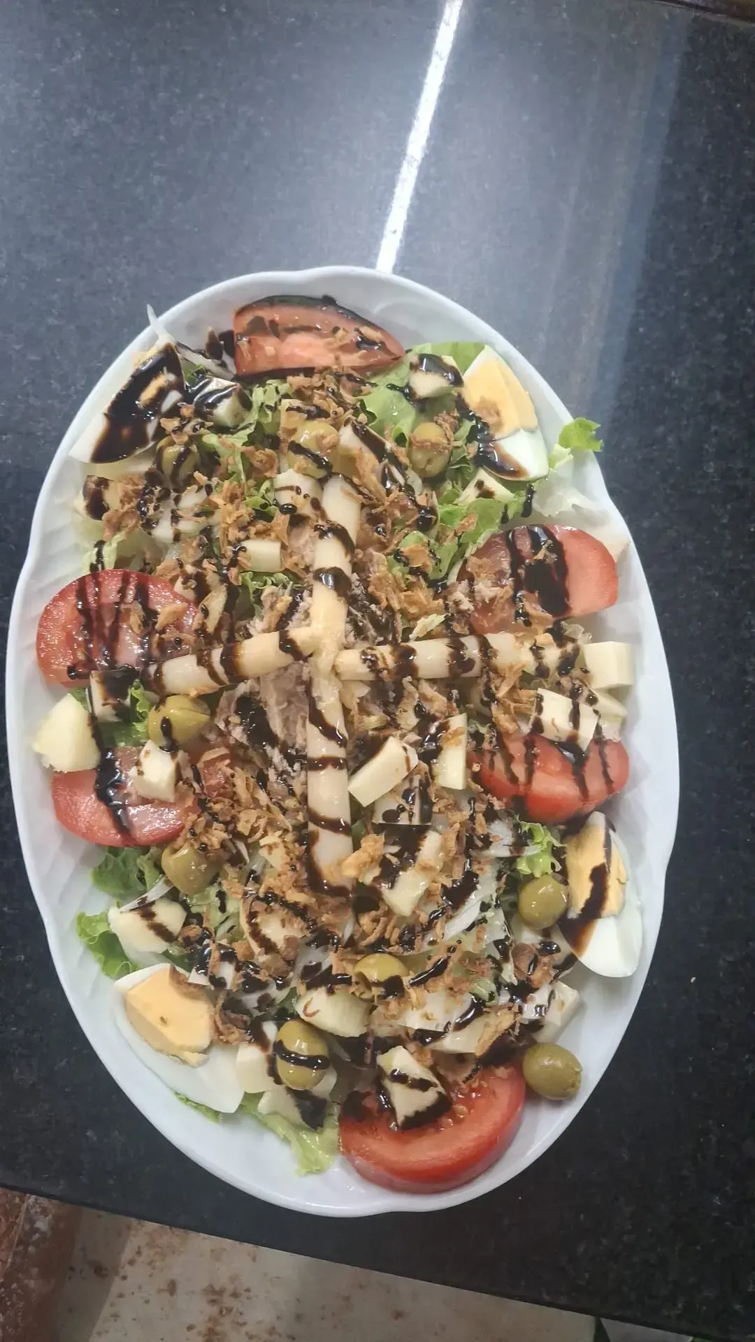 Ensalada ovalada con tomates, aguacate, huevos, picatostes y un aderezo oscuro.