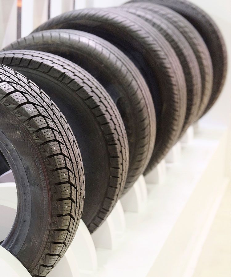 Fila de neumáticos negros exhibidos en un estante blanco, con patrones de banda de rodadura visibles.