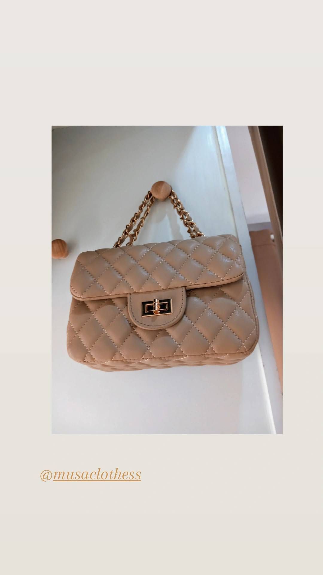Un bolso beige con una cadena dorada está colgado en una pared.