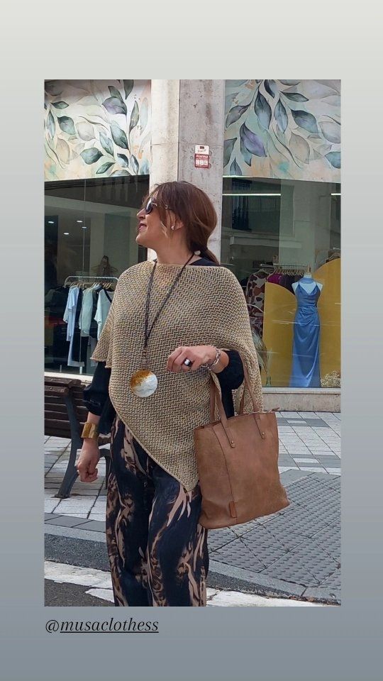 Una mujer que lleva un poncho y una bolsa marrón camina por la calle.