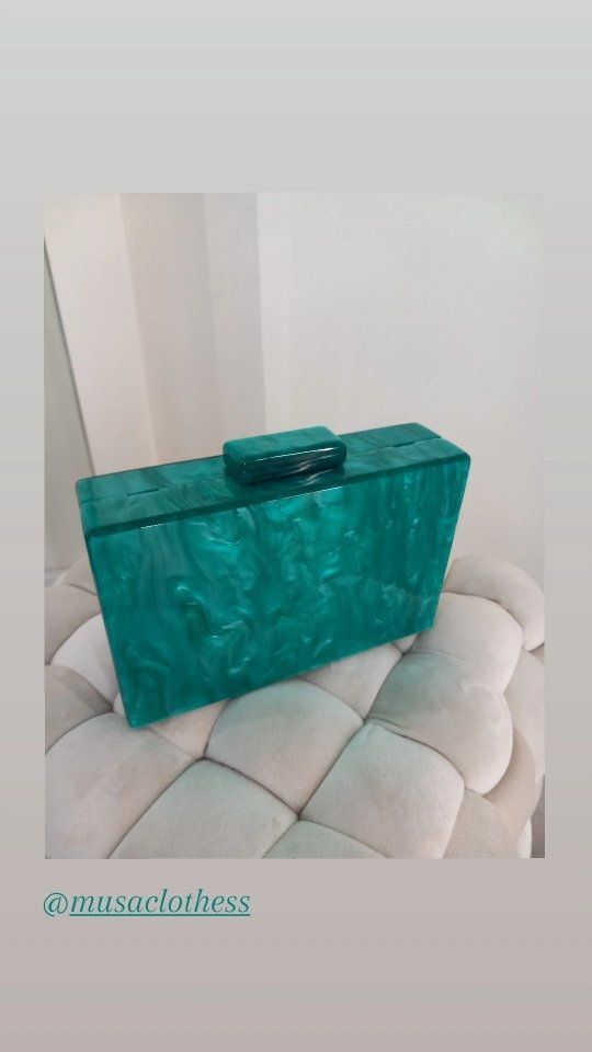 Un bolso de mano verde reposa encima de un sofá blanco.