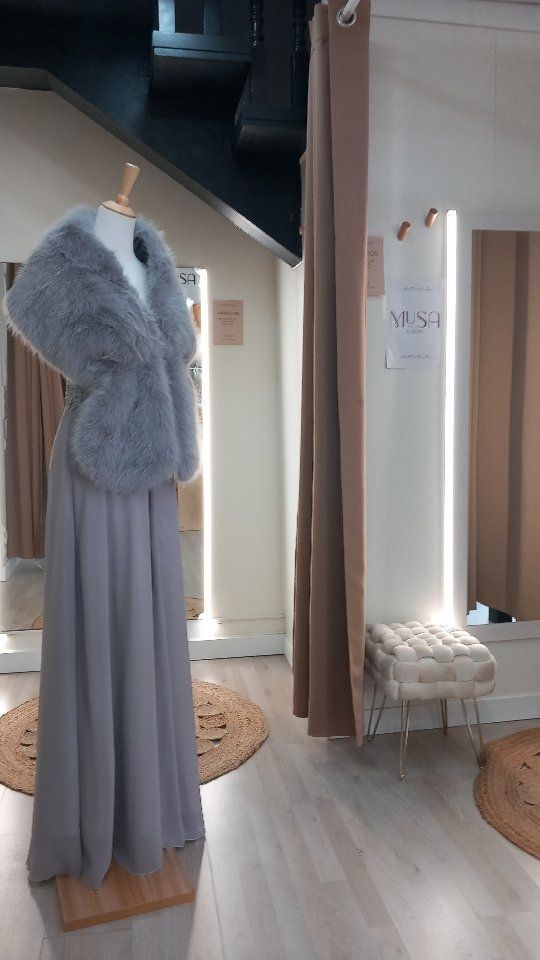 Un maniquí lleva un vestido gris y un chal de piel en un probador.