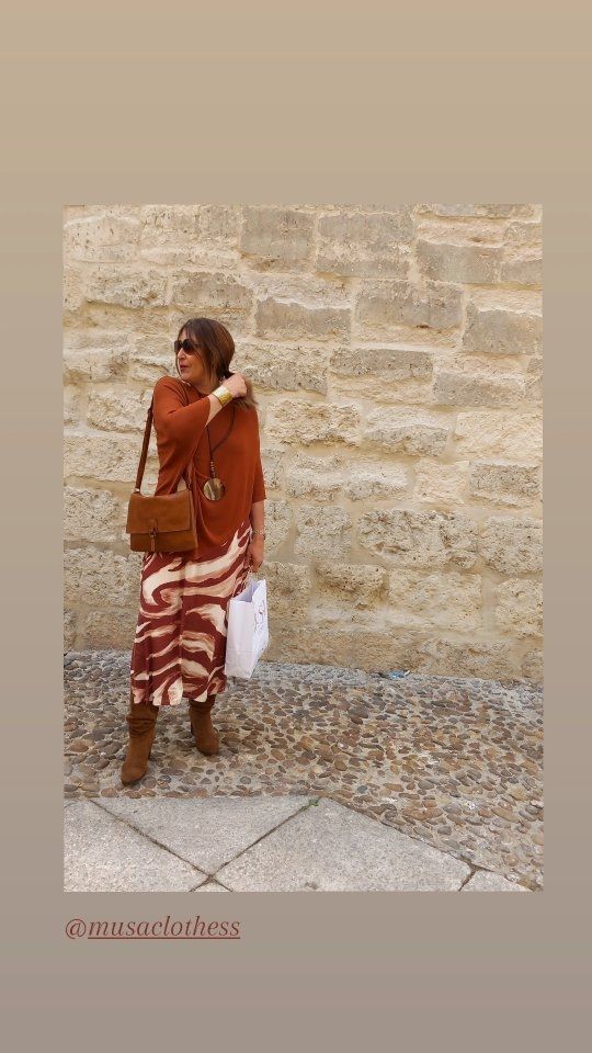 Una mujer está parada frente a una pared de ladrillos sosteniendo una bolsa.
