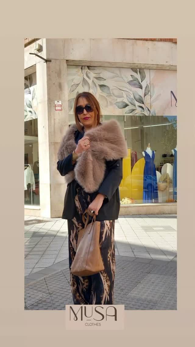 Una mujer que lleva un chal de piel y gafas de sol está parada frente a una tienda.