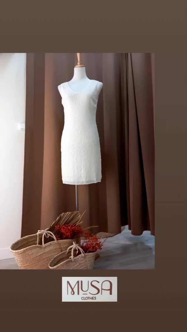 Un vestido blanco está sobre un maniquí delante de una cortina marrón.