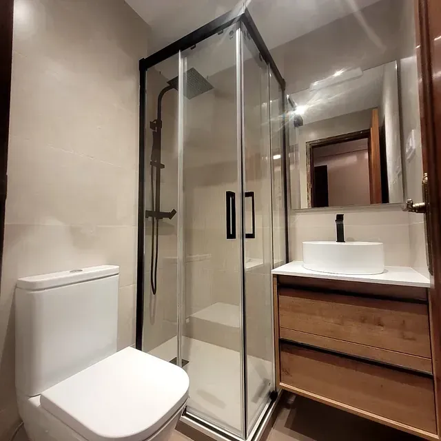 Reforma de baño en Madrid, azulejos color beige, sanitarios Roca, mampara y grifería negras.