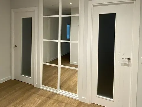 Un pasillo con dos puertas y un espejo en la pared.