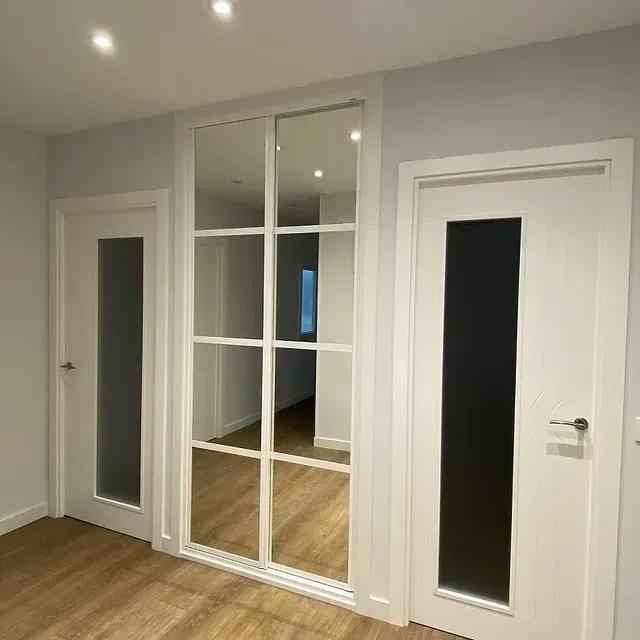 Reforma de vivienda en Madrid, pasillo con dos puertas lacadas blancas, un armario con gran espejo y tarima laminada