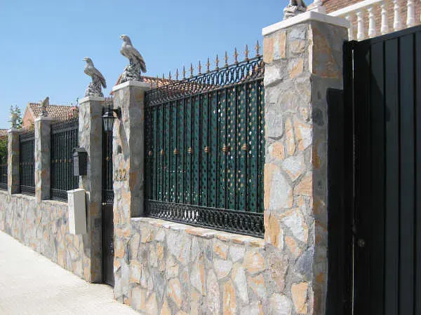 reforma de vivienda en Madrid de  muro de piedra con una puerta negra de hierro y una valla de hierro forjado.