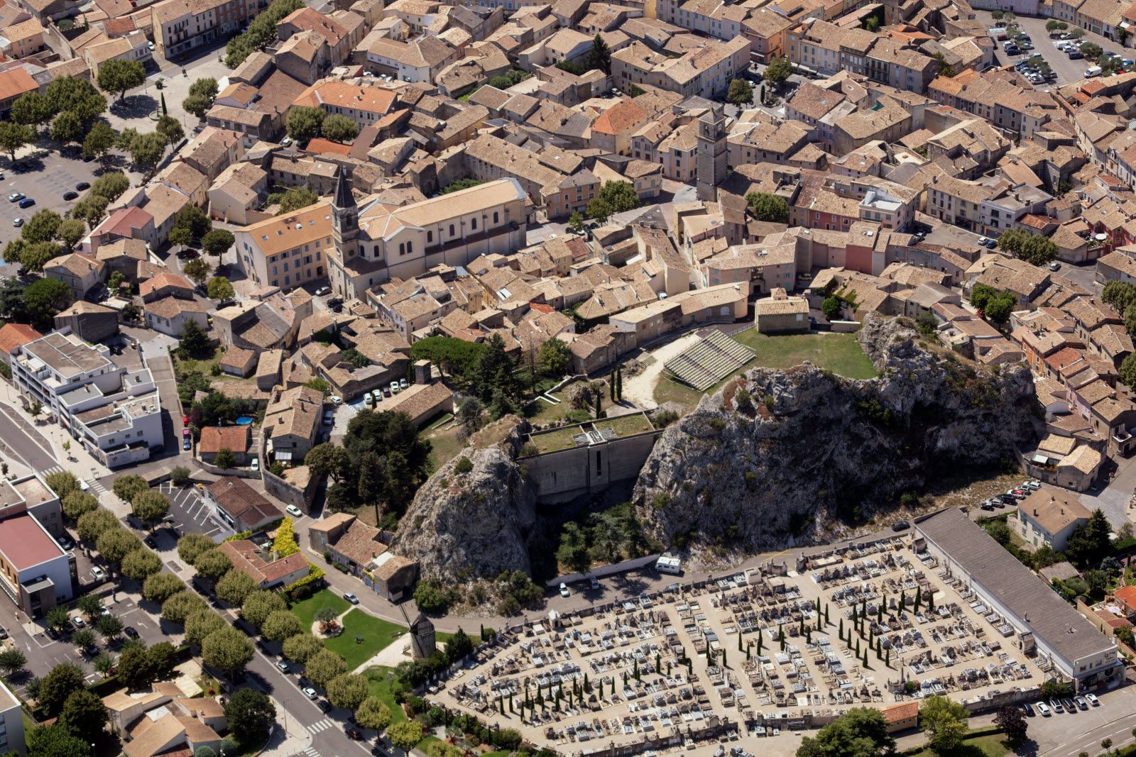 Vue aérienne d'une ville aux bâtiments en pierre et au centre dominé par un imposant promontoire rocheux. Un cimetière se trouve au premier plan.