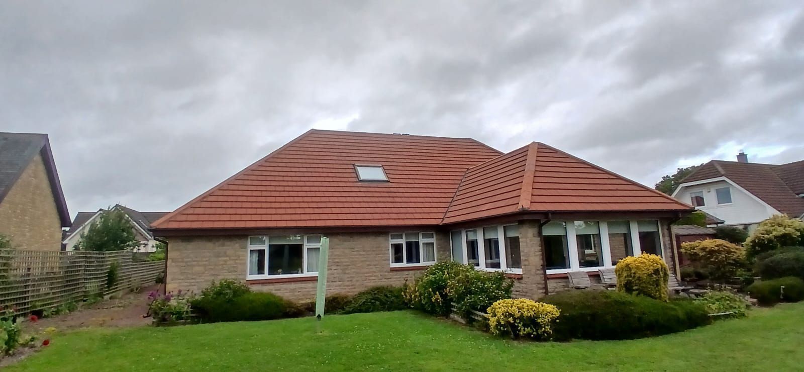 Single-story brick house with red tile roof and green lawn on a cloudy day