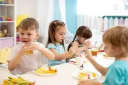 Un grupo de niños está sentado en una mesa comiendo comida y bebiendo jugo.