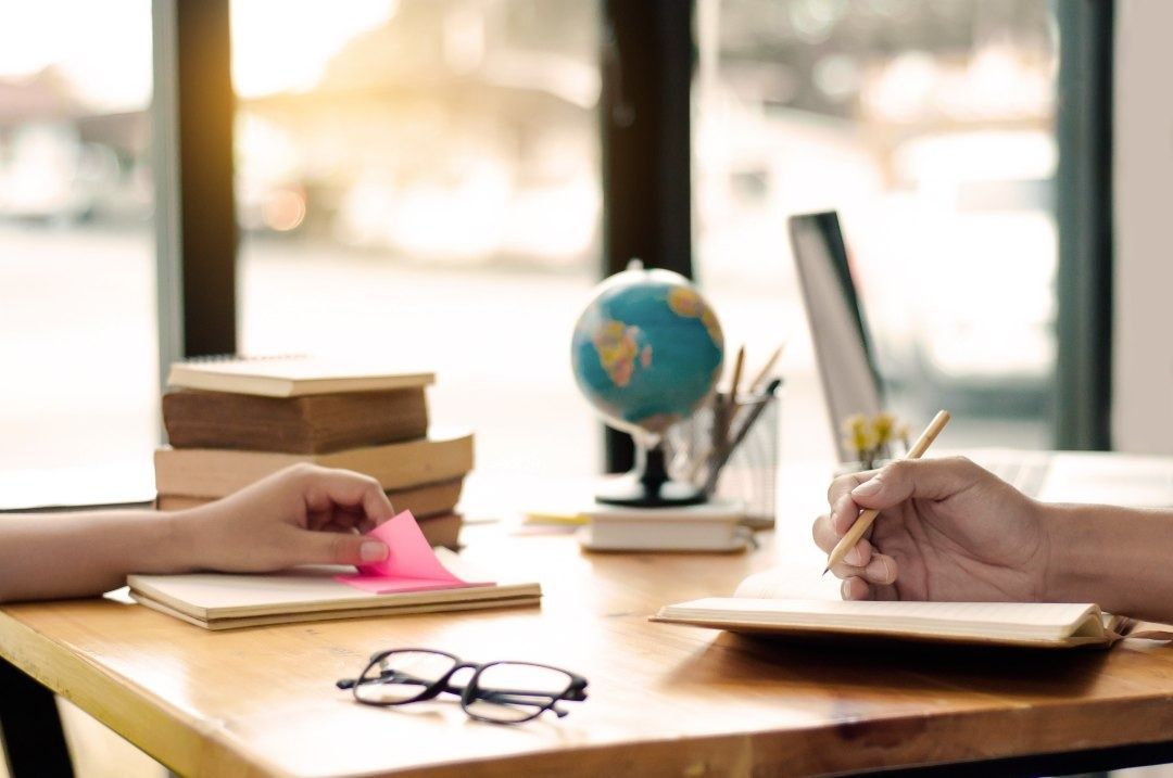 Una persona está sentada en un escritorio escribiendo en un cuaderno.