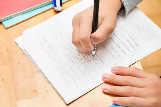 Una persona está escribiendo en un trozo de papel con un lápiz.
