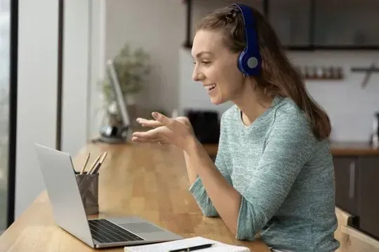Una mujer que usa auriculares está sentada en una mesa utilizando una computadora portátil.