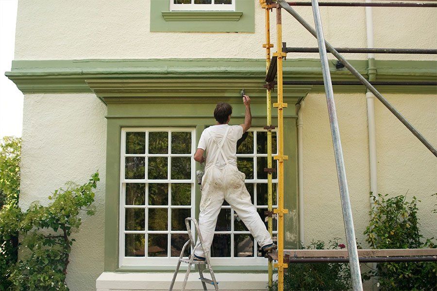 Un homme en train de repeindre la façade d'une maison en vert