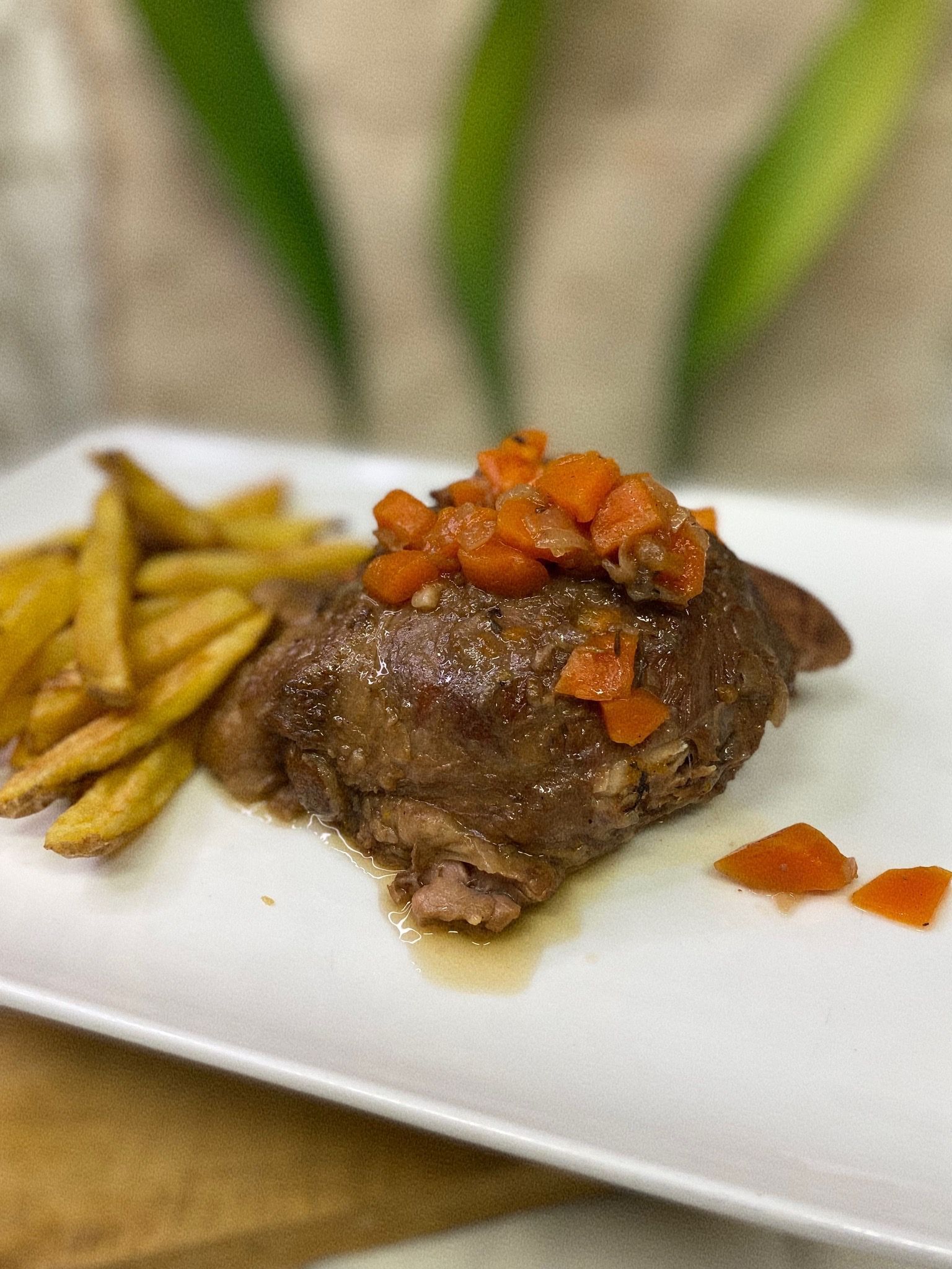 Un plat blanc amb un tros de carn i patates fregides per sobre.