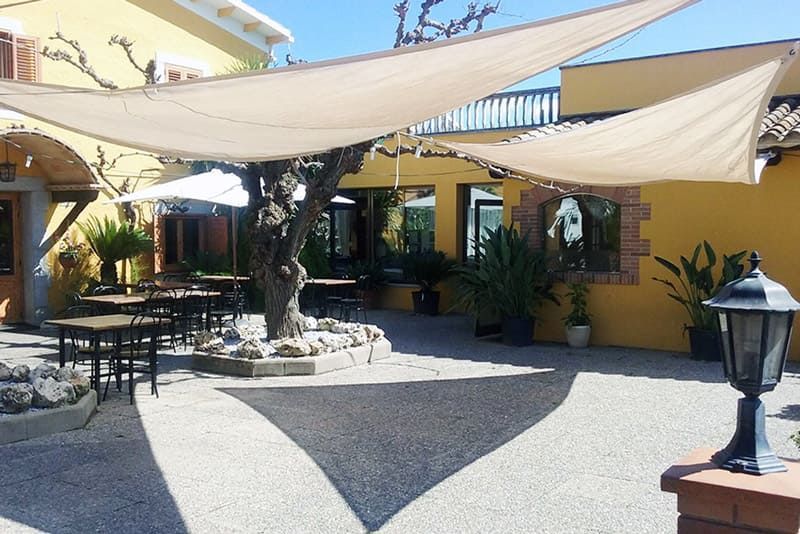 Un pati amb taules i para-sols davant d'un edifici groc