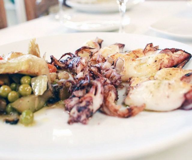 Un plat blanc amb calamars i verdures sobre una taula.