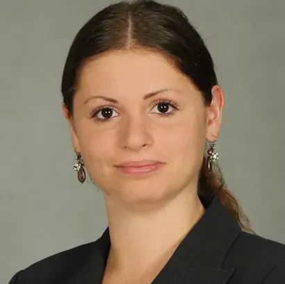 Mujer con cabello oscuro, con aretes, con blazer oscuro y mirando directamente a la cámara.