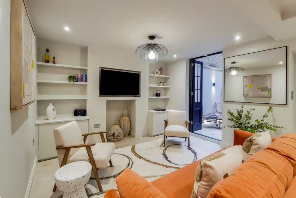 Living room with orange sofa, white chairs, TV, and open doorway to patio.