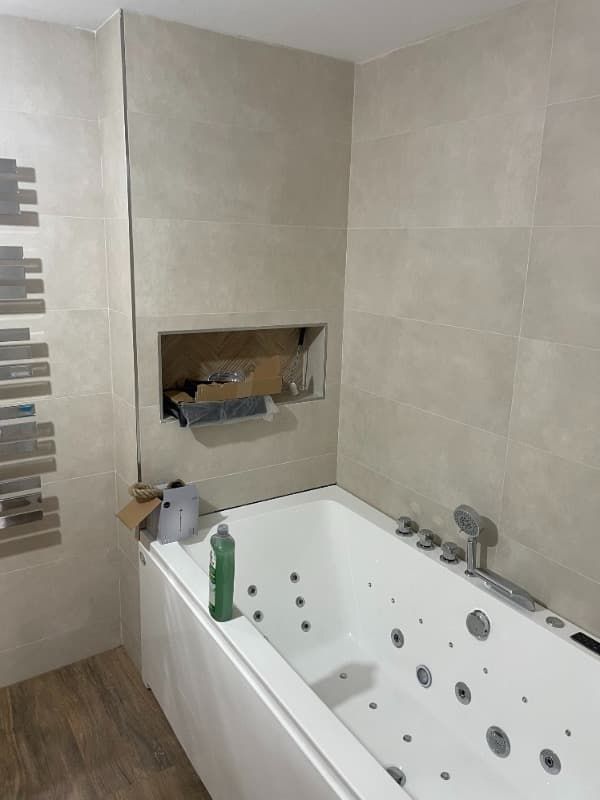 Baño con pared parcialmente alicatada, bañera con chorros y estantería empotrada en construcción.