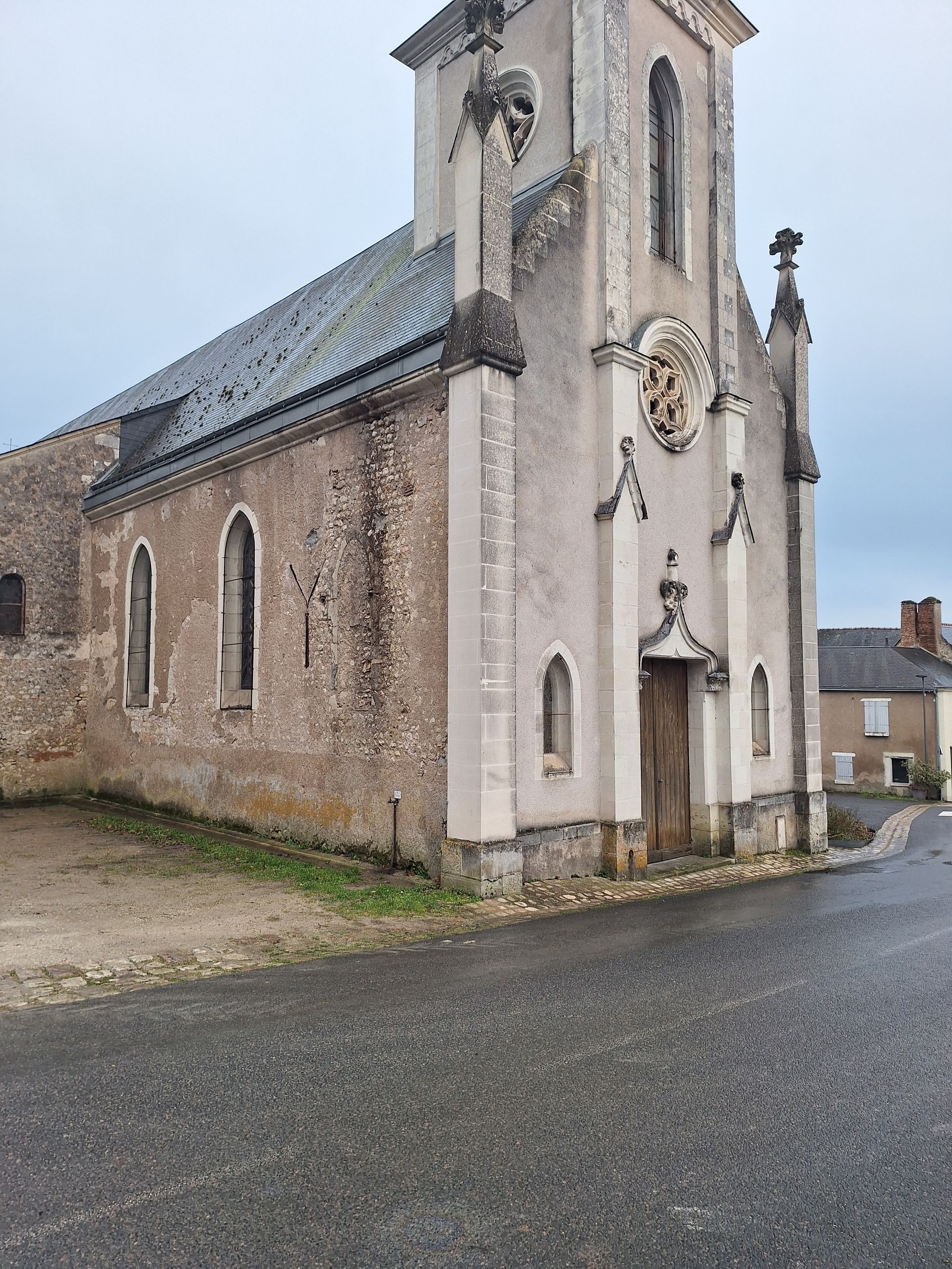 Église en pierre au toit gris, aux petites fenêtres et à la porte en bois, par temps nuageux.