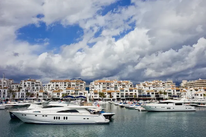 Un grupo de barcos están atracados en un puerto con edificios al fondo.
