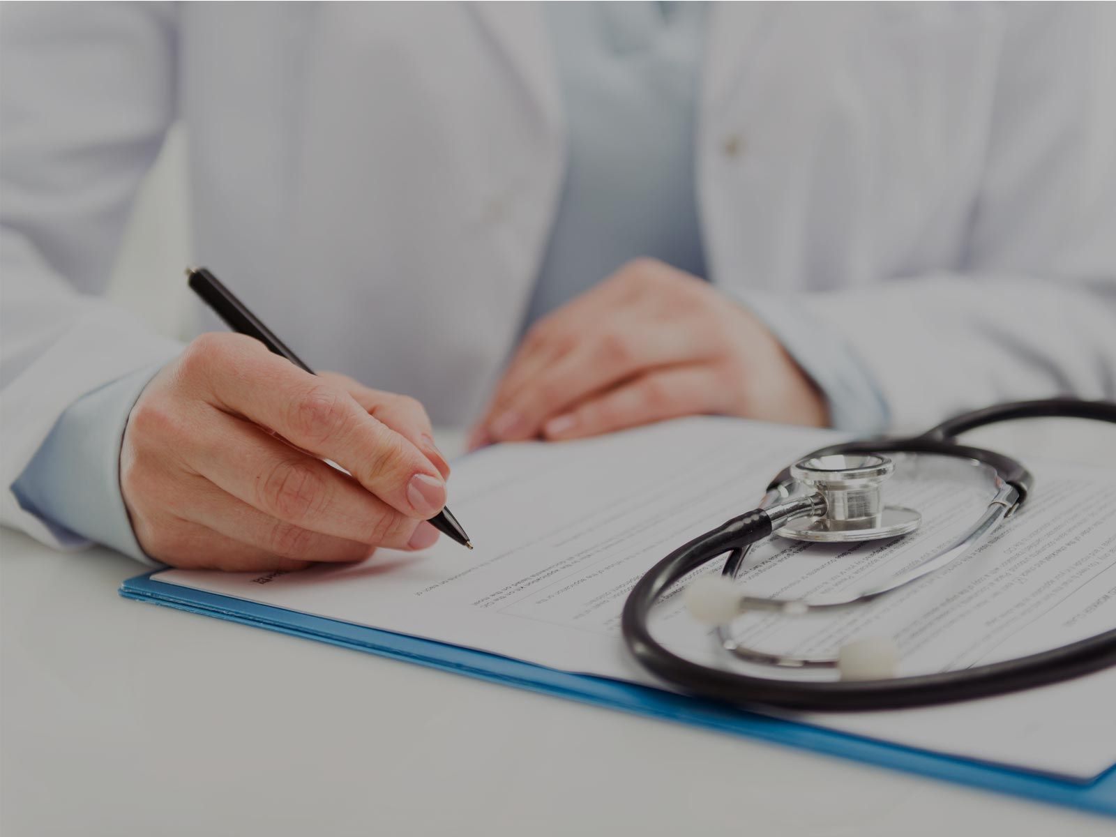 Un médico está escribiendo en un portapapeles al lado de un estetoscopio.