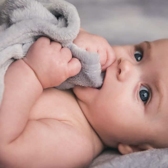 Un bebé está acostado en una cama con una manta en la boca.