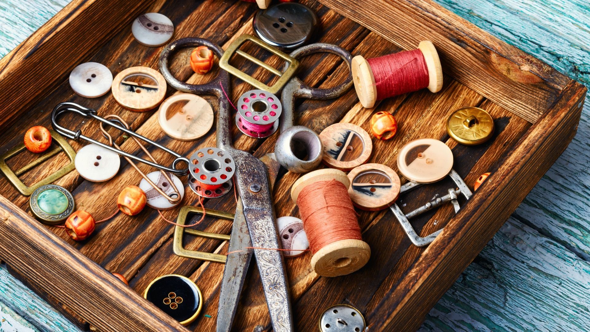 Una bandeja de madera llena de botones, carretes de hilo, tijeras y otros artículos de costura.