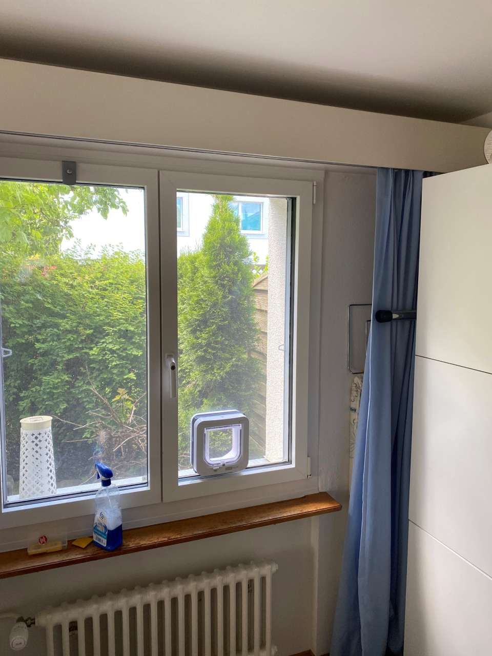 Une pièce avec une fenêtre, un radiateur et des rideaux bleus.