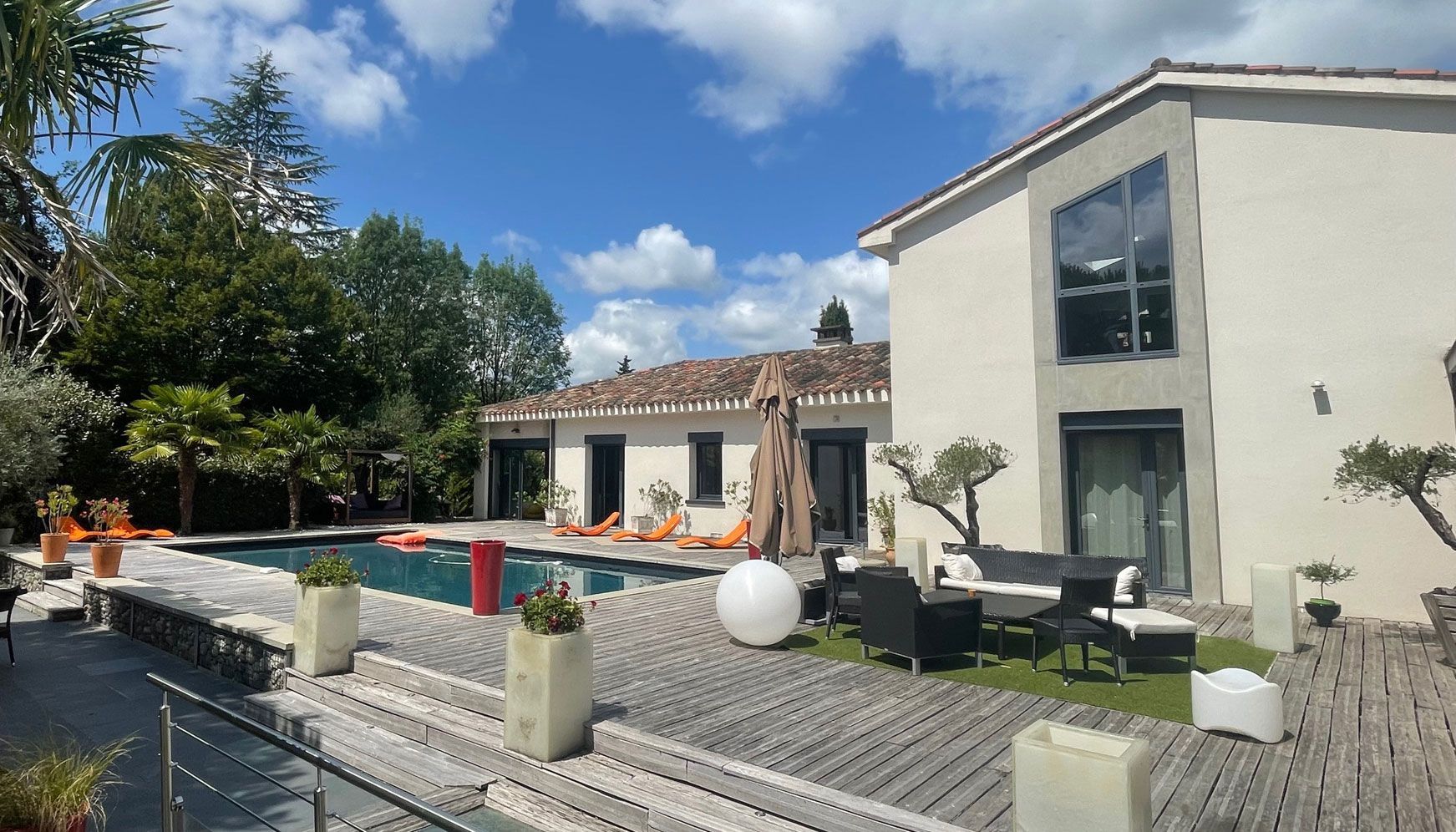 Maison moderne avec piscine et mobilier de terrasse, journée ensoleillée, ciel bleu.