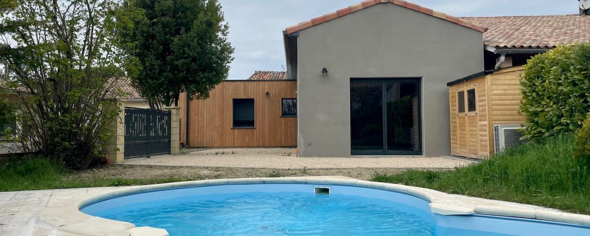 Une maison avec une piscine dans le jardin. La maison est gris clair avec un toit rouge.