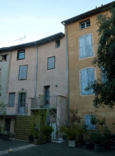 Des immeubles aux façades rose pastel et jaune, aux volets bleus et aux petits balcons, dans un cadre européen.